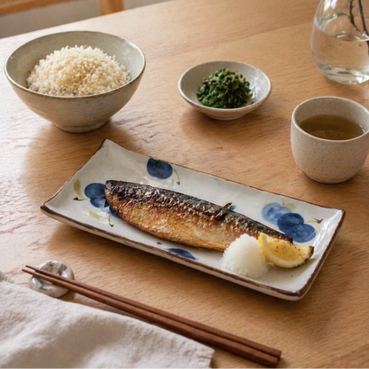 Dining table with a plate of fish, bowl of rice, and cup of tea.