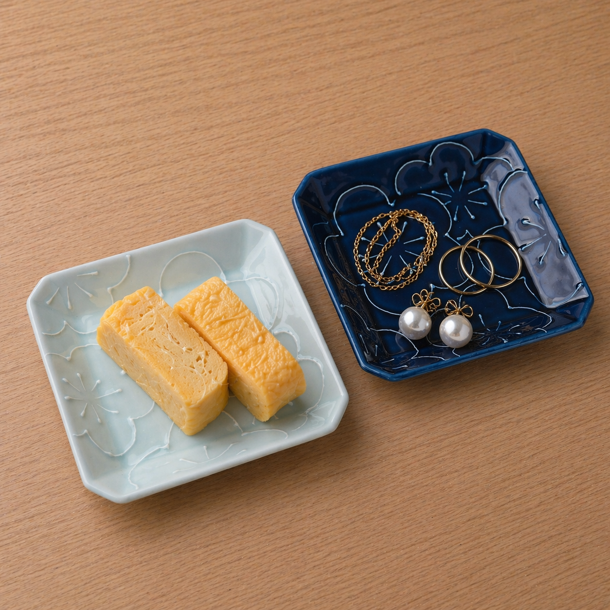 Two pieces of yellow food on a white plate next to a blue jewelry dish with earrings and necklaces on a wooden surface.