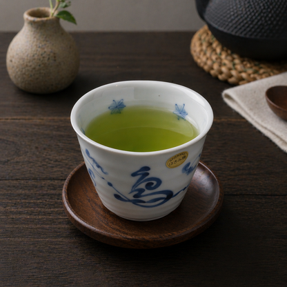 White ceramic cup with blue floral patterns filled with green tea, placed on a wooden coaster on a dark wooden table.
