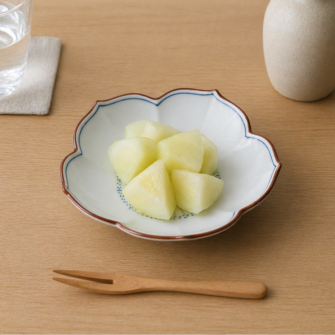 Diced fruit in a decorative bowl on a wooden table with a glass of water and a vase.