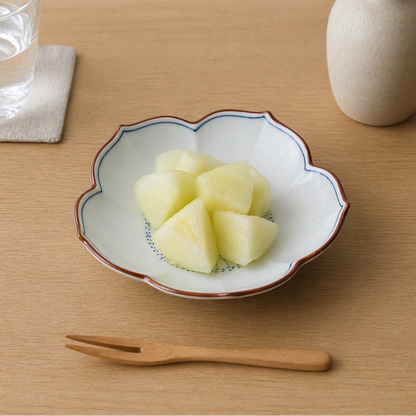 Diced fruit in a decorative bowl on a wooden table with a glass of water and a vase.
