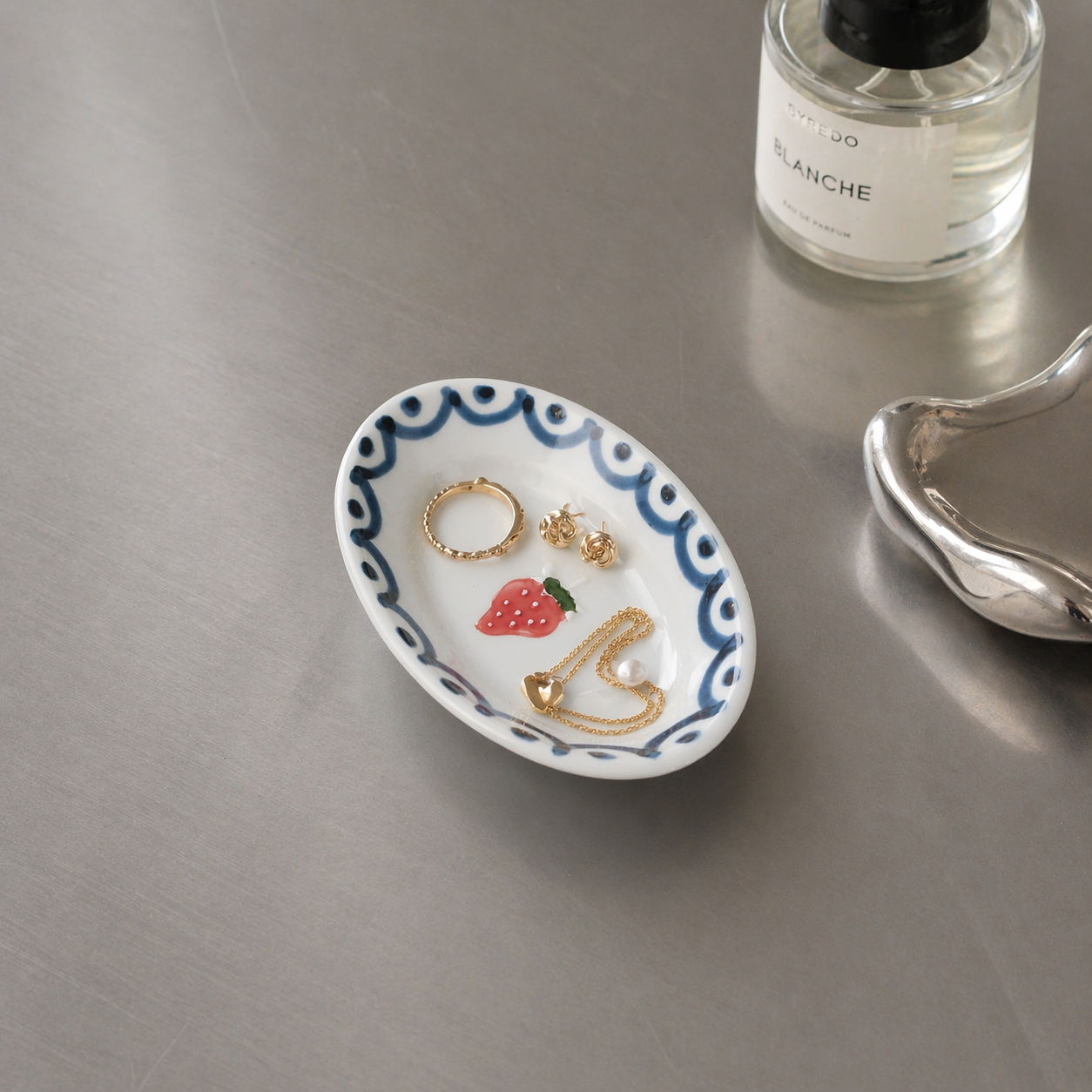 Jewelry dish with rings on a metallic surface next to a bottle of perfume.
